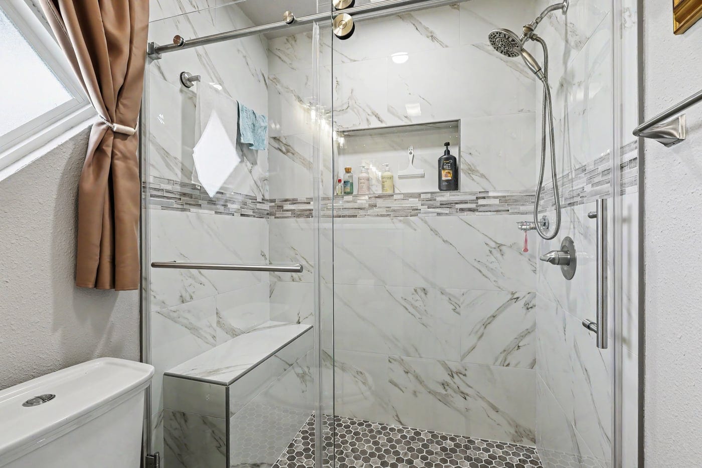 Walk-in shower with marble-look tile, mosaic accent band and glass door